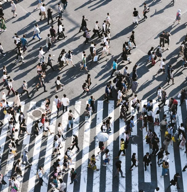 Bird's-eye view of many pedestrians crossing a wide intersection, forming geometric patterns.