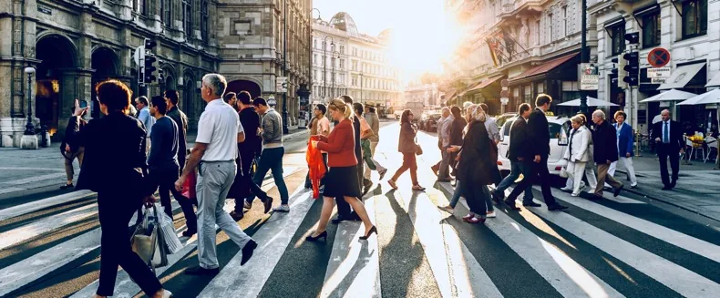 Pedestrians crossing a wide sunlit street at golden hour.